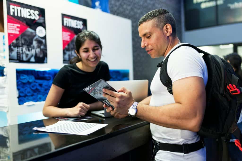 Fitness franchise check in desk with two people at counter. One behind and one checking in with membership card